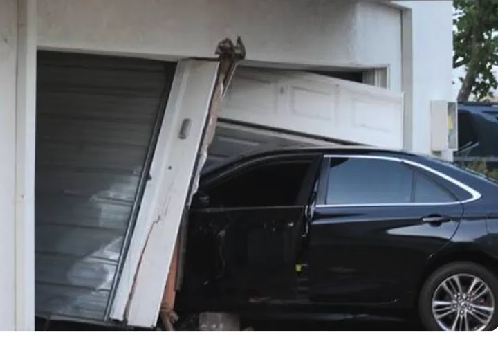 Black sedan crashed through a garage door, with the door panels torn from the opening