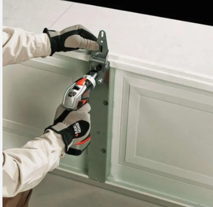 Technician fastening a garage door hinge to a white panel with a cordless drill