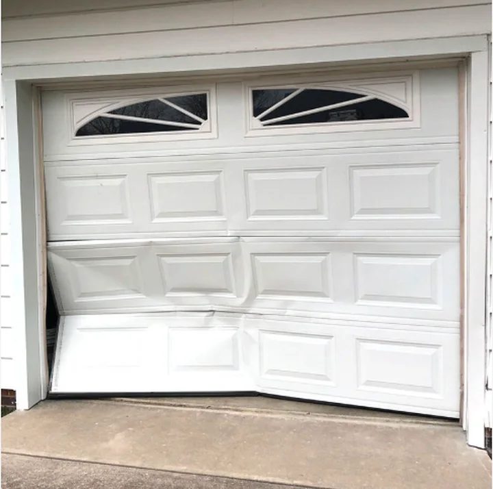 White raised-panel garage door with sunburst windows and crumpled lower sections that need replacing