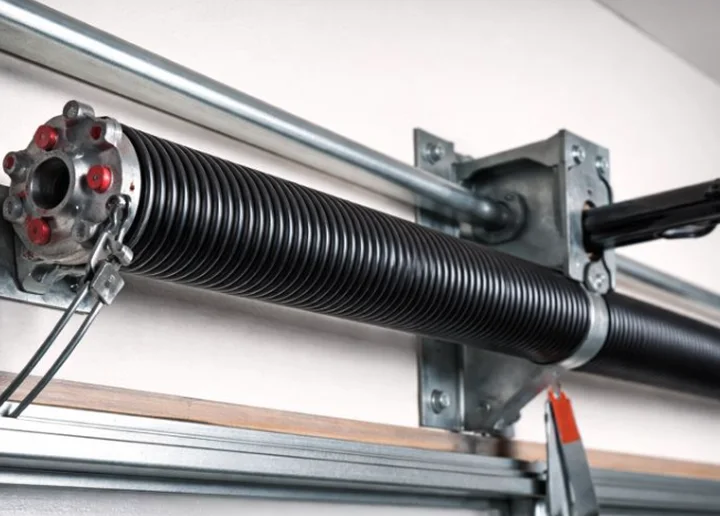 Black torsion spring on the winding bar above a garage door, with the winding cone and lift cables visible